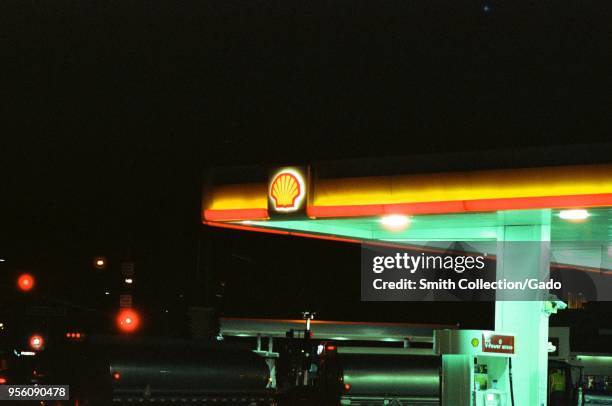 Close-up of a Shell gas station with sign and logo visible at night, with gasoline trucks parked near fuel pumps, Dublin, California, March 5, 2018.