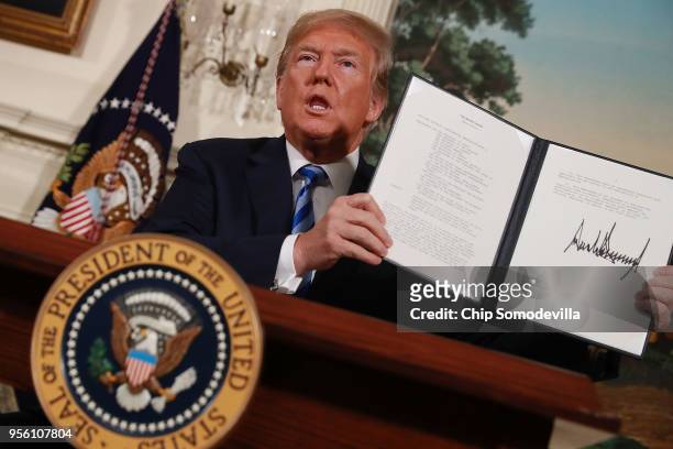 President Donald Trump holds up a memorandum that re-instates sanctions on Iran after he announced his decision to withdraw the United States from...