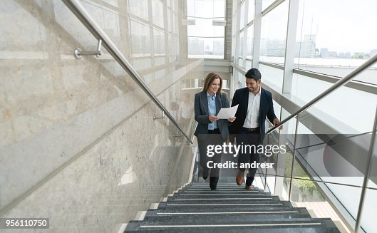 Business partners walking up the stairs to the office looking at a document very satisfied Business partners walking up the stairs to the office looking at a document very satisfied