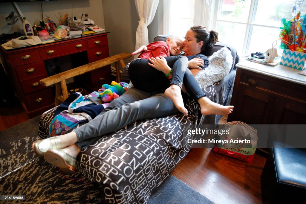 A mother and daughter with cancer happily embrace one another on the couch, in the living room.