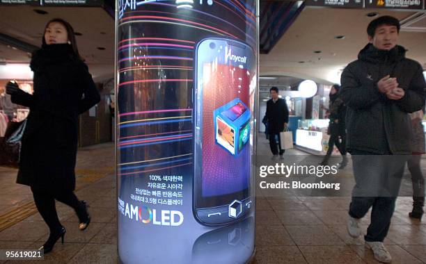 Pedestrians walk past an advertisement for Samsung Electronics Co.'s Anycall brand mobile phones at a subway station in Seoul, South Korea, on...