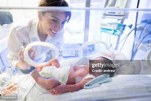 schöne mutter betrachten ihr frühgeborenes im inkubator auf der intensivstation - premature baby incubator stock-fotos und bilder