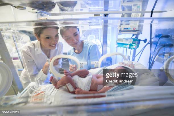 愛情深い母親と酸素でインキュベーターで生まれたばかりの赤ちゃんを見て、新生児の集中治療室での看護師 - 新生児集中治療室 ストックフォトと画像