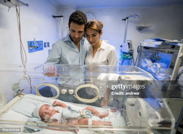 pareja abrazándose en unidad de cuidados intensivos neonatal del hombre mientras ambos miran a su hijo recién nacido - premature baby incubator fotografías e imágenes de stock