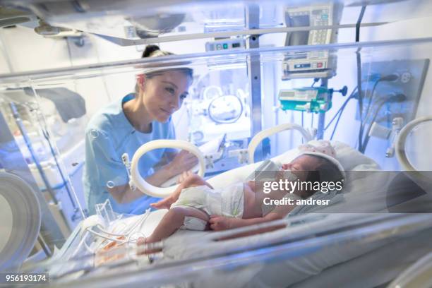 hermosa enfermera comprobar a un bebé prematuro en la unidad de cuidados intensivos neonatales tomando notas en un portapapeles - premature baby incubator fotografías e imágenes de stock