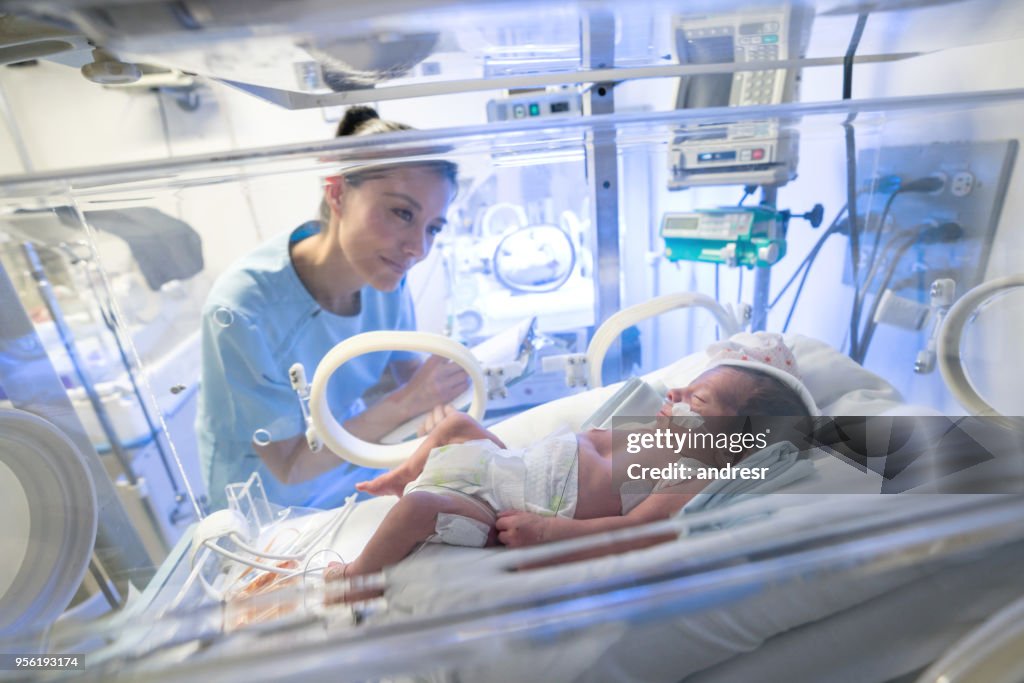 Vacker sjuksköterska kontrollera en prematur baby i neonatal intensivvårdsavdelning anteckningar på ett urklipp