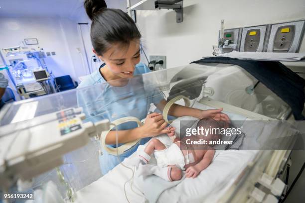 schöne neugeborenes baby im brutkasten krankenschwestern finger zu halten, während sie lächelt - nicu stock-fotos und bilder