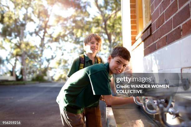 australian school children drinking from water fountain in playground - thisisaustralia stock-fotos und bilder