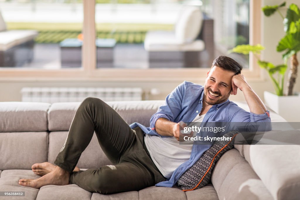 Cheerful man changing channels while relaxing on sofa at home.