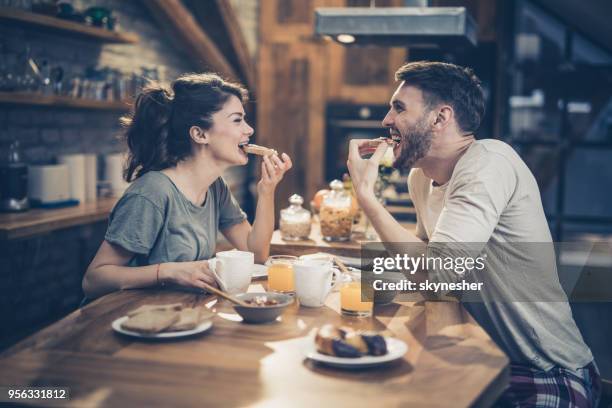 jonge gelukkige paar plezier terwijl het eten van broodjes voor het ontbijt in de keuken. - eating food happy stockfoto's en -beelden