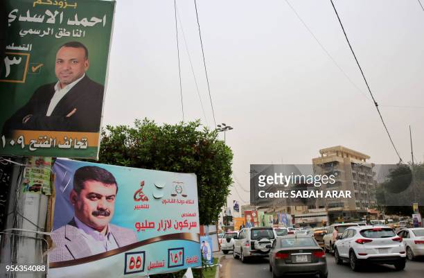 Traffic drives past osters bearing portraits of candidates in Iraq's upcoming parliamentary elections in Baghdad on May 8, 2018. Arabic caption reads...