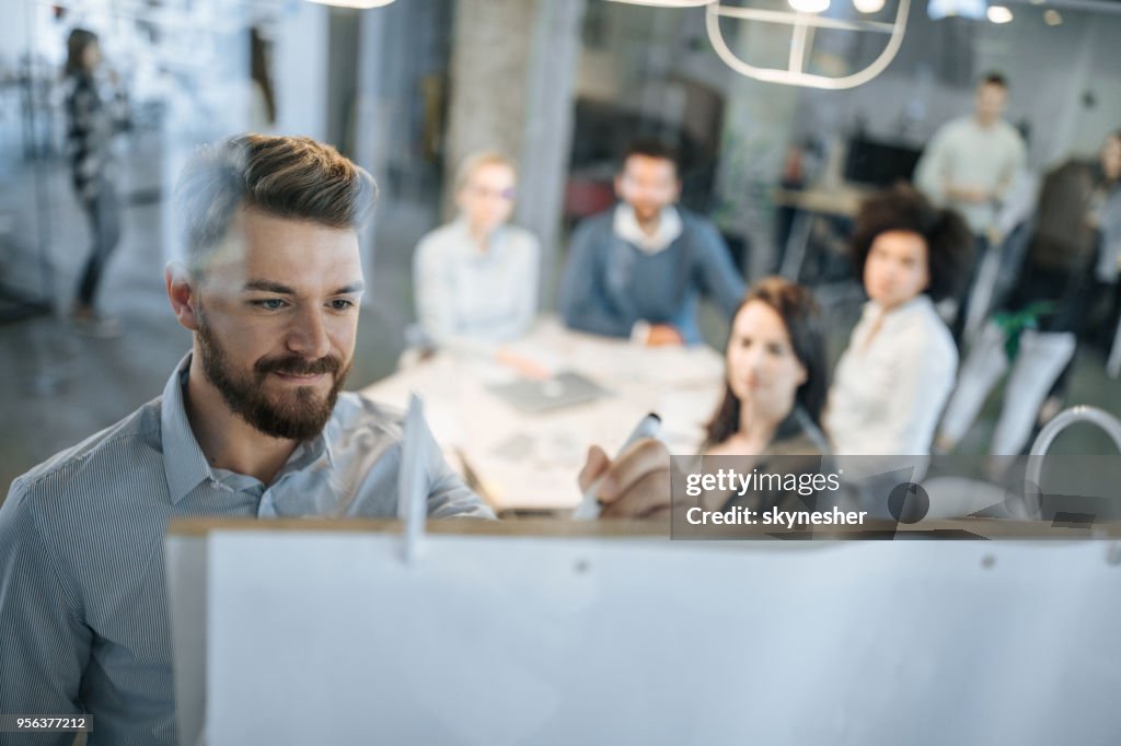 Young businessman writing ideas on whiteboard during a meeting with his colleagues.