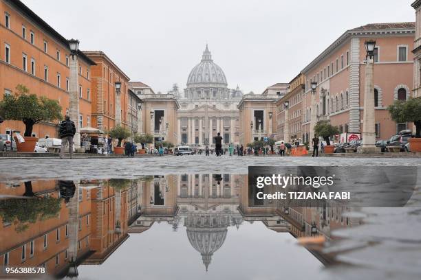 St Peter's basilica reflects in a puddle of Via della Conciliazione on May 9, 2018 in Rome.