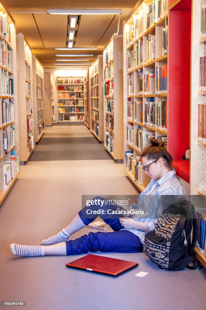 Jovem estudante feminino usando o celular na biblioteca
