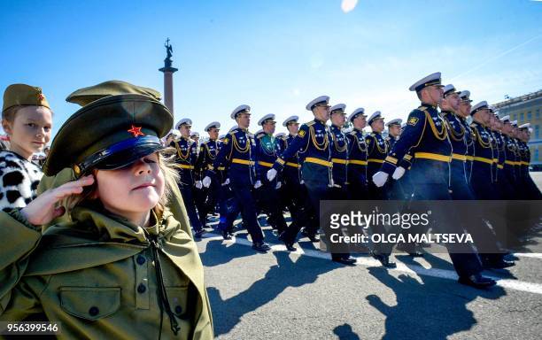 Girl dressed in a Soviet Army styled uniform salutes as Russian military personnel march at Dvortsovaya Square during the Victory Day military parade...