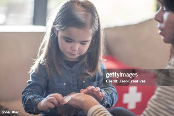girl sticking plaster onto mothers hand - verbandskasten stock-fotos und bilder