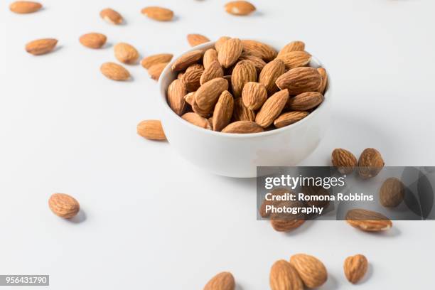 almond nuts in bowl and on white background - mandeln stock-fotos und bilder