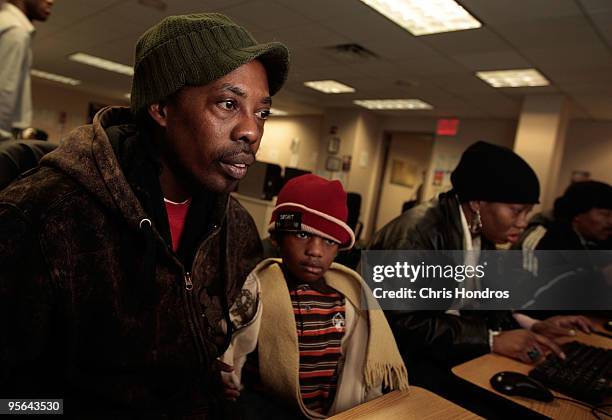 Job seeker Anderson Vilceus of Brooklyn looks over online job postings while holding his son, Anderson Vilceus Jr., in the New York State Labor...