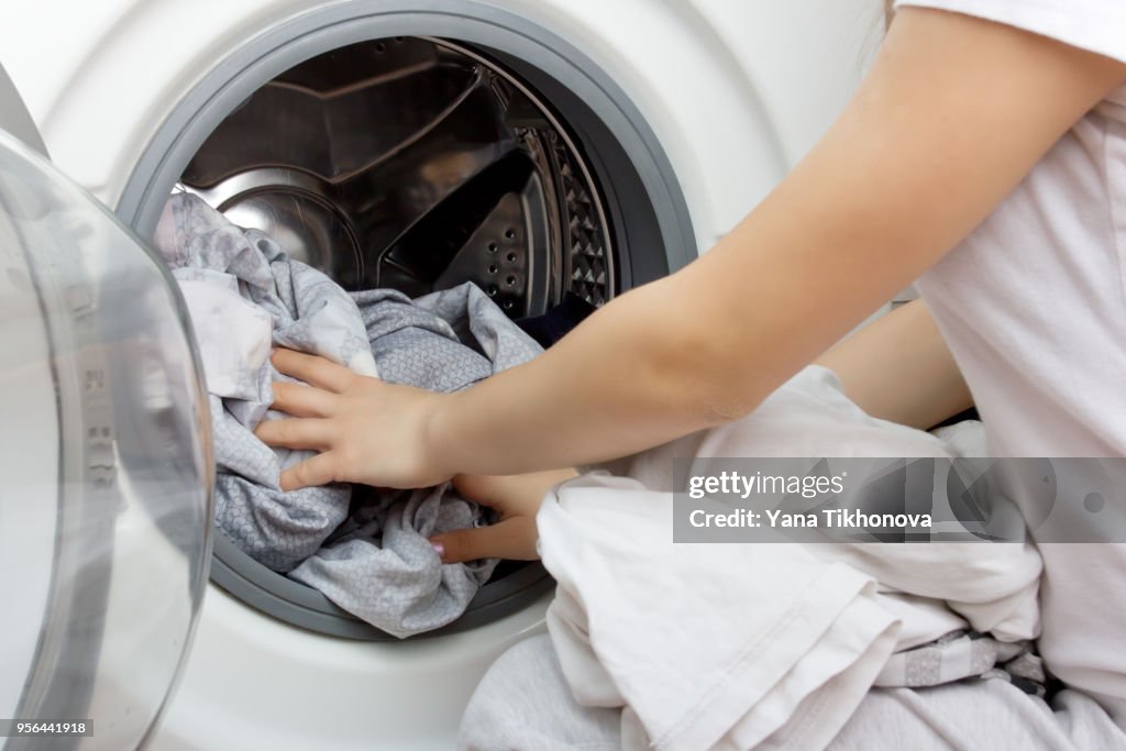 Hands of a young girl put clothes in the washing machine drum