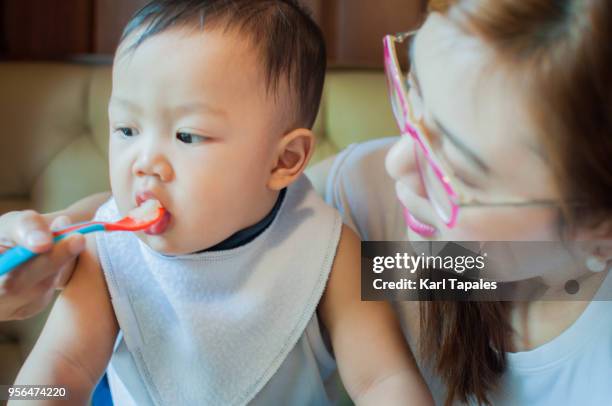 a mother is feeding her son with a solid food - filipino family eating stock pictures, royalty-free photos & images