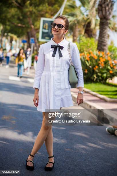 Guest, wearing a white dress with black bow tie and Armani light green bag, is seen in the streets of Cannes during the 71st annual Cannes Film...