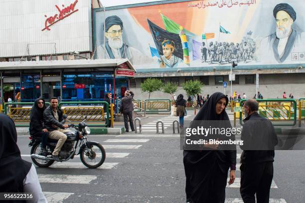 Women cross a street near a giant political mural depicting Ayatollah Ali Khamenei, Iran's supreme leader, left, and Ruhollah Khomeini, founder of...