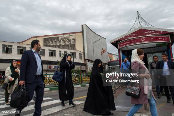 Pedestrians cross a street near a mural on the wall of a movie theatre showing men holding posters of Ayatollah Khomeini, former leader of Iran, in...