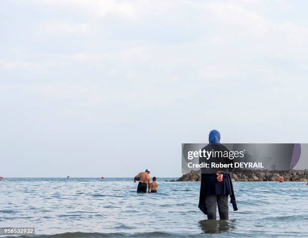 Une femme musulmane habillée, les pieds dans l'eau, regarde sa famille se baigner dans la mer, 11 juillet 2016 Carnon, Hérault, France.