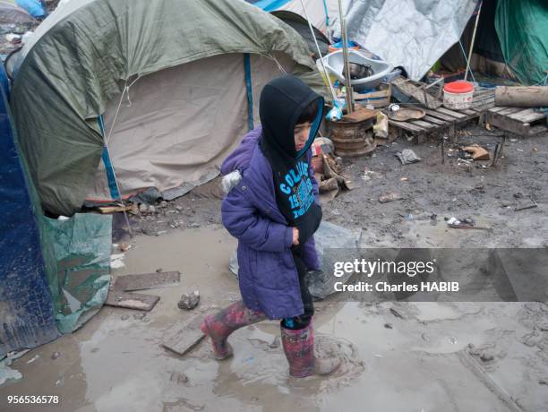 Enfant marchant dans la boue avec des bottes, camp de réfugiés, le 16 février 2016, Dunkerque, France.