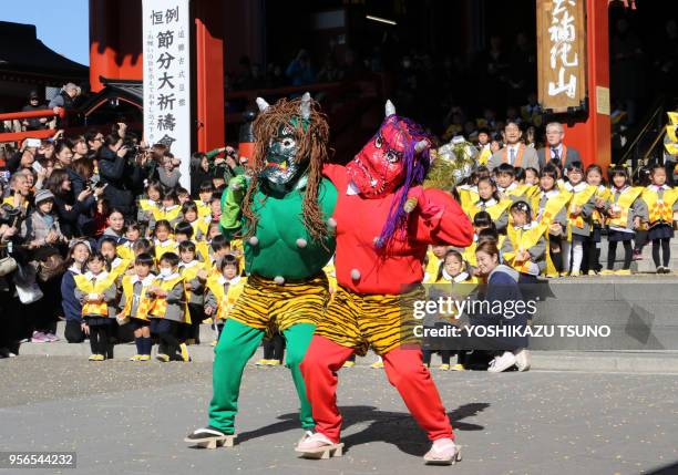 Mothers of kindergarten children, wearing demon-like masks to scare pupils, take part in a traditional bean-throwing ceremony to drive away evils and...