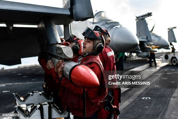 Crew members of US aircraft carrier USS Harry S Truman lift a missile into place on the wing of an F18 Hornet fighter jet on the flight deck of the...