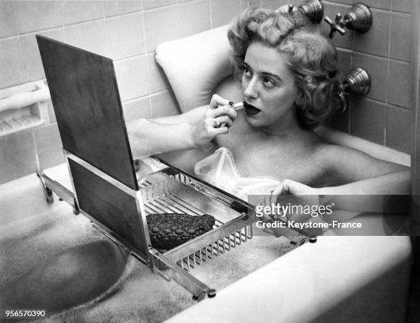Midge Gibson, de l'institut de modèles, profite d'un moment de détente dans son bain en se mettant du rouge à lèvres face à un miroir reposant sur un...