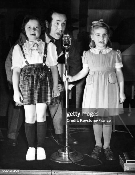 Le chanteur Bob Russell donne un cours de chant à deux petites filles dans une garderie d'enfants à New York City, Etats-Unis en octobre 1945.