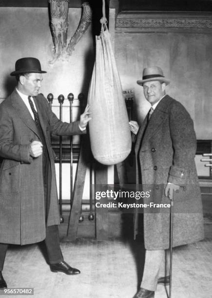 Le boxeur Jack Dempsey s'entraîne sur un sac de frappe sous l'oeil attentif de Tex Rickard, Roi des Promoteurs, au gymnase McLevy, circa 1930 à New...