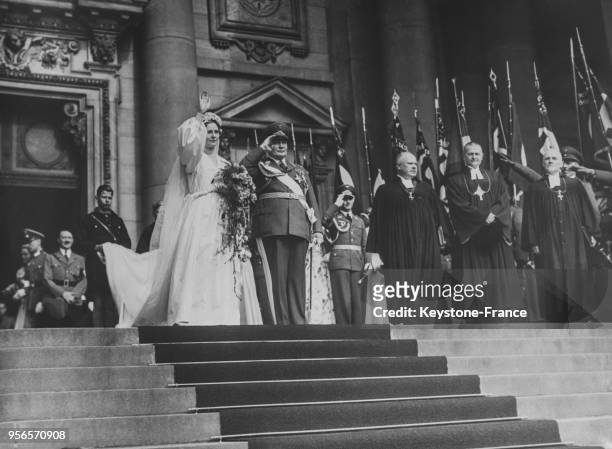 Après la cérémonie religieuse, les mariés sortent de la cathédrale et saluent la foule qui les acclame, au fond, le Chancelier Hitler, témoin des...