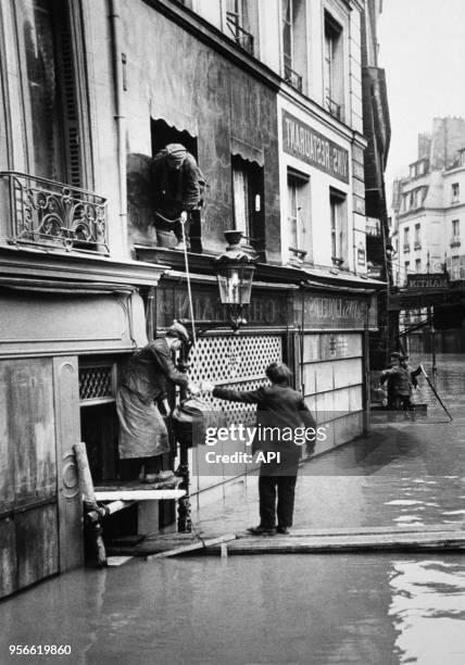 Des Parisiens évacuent leurs habitations en marchant sur des planches flottant sur l'eau lors de la crue de la Seine en 1910 à Paris, France.