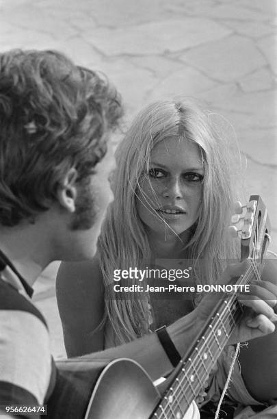 Brigitte Bardot et Johnny Hallyday jouant de la guitare sur une plage en août 1967 à Saint-Tropez, France.