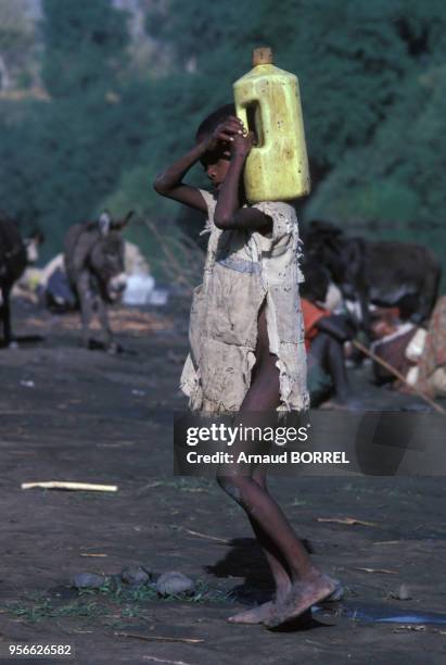 Enfant soudanais en haillons portant un bidon sale lors d'une famine dans l'est du pays en janvier 1985 au Soudan.