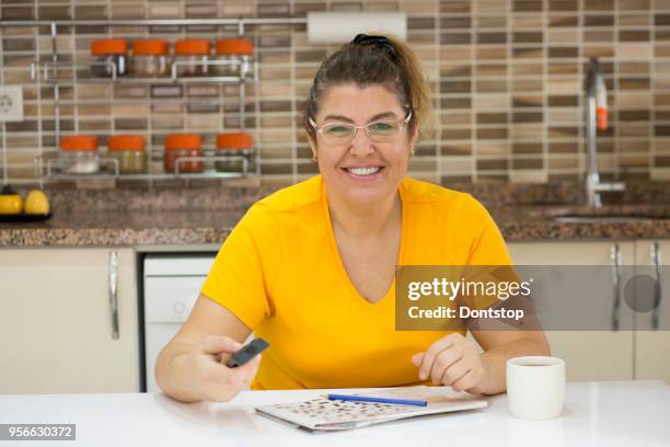 smiling woman holding a pencil and solves crossword puzzle - crossword stock pictures, royalty-free photos & images