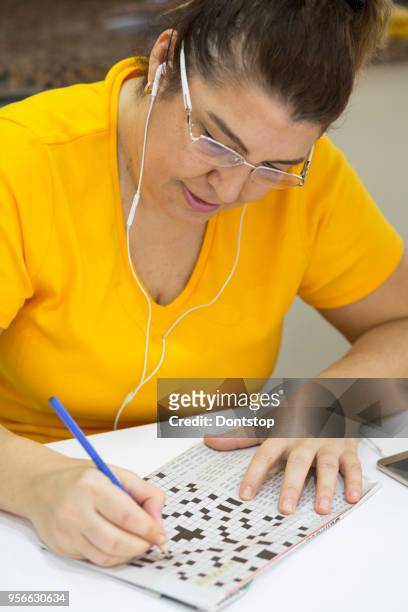smiling woman holding a pencil and solves crossword puzzle - crossword stock pictures, royalty-free photos & images