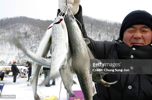 South Korean man displays a fish caught through a hole into a frozen river during a contest to catch Mountain Trout on January 9, 2010 in...