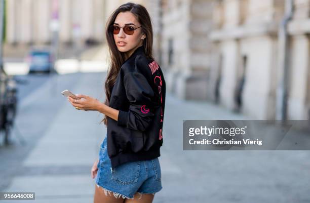 Model Dora Molina wearing denim shorts and black one piece Urban Outfitters, Quay sunglasses, Just Fabulous boots, jacket with printing Voodoo doll...