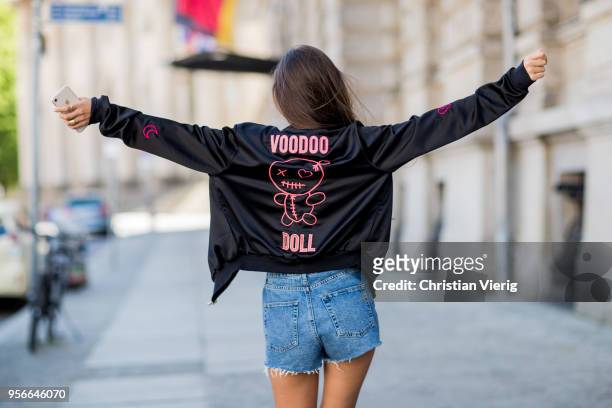 Model Dora Molina wearing denim shorts and black one piece Urban Outfitters, Quay sunglasses, Just Fabulous boots, jacket with printing Voodoo doll...