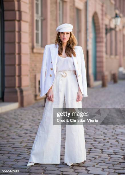 Alexandra Lapp wearing a white cotton blazer with gold buttons by Balmain, linen Palazzo pants with a high waist belt in white by Zimmermann, a white...