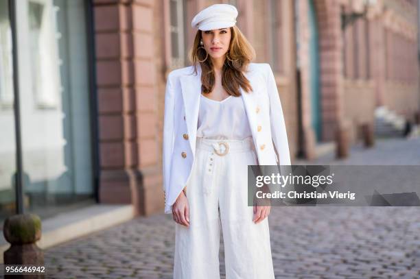 Alexandra Lapp wearing a white cotton blazer with gold buttons by Balmain, linen Palazzo pants with a high waist belt in white by Zimmermann, a white...