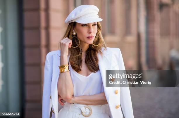 Alexandra Lapp wearing a white cotton blazer with gold buttons by Balmain, linen Palazzo pants with a high waist belt in white by Zimmermann, a white...