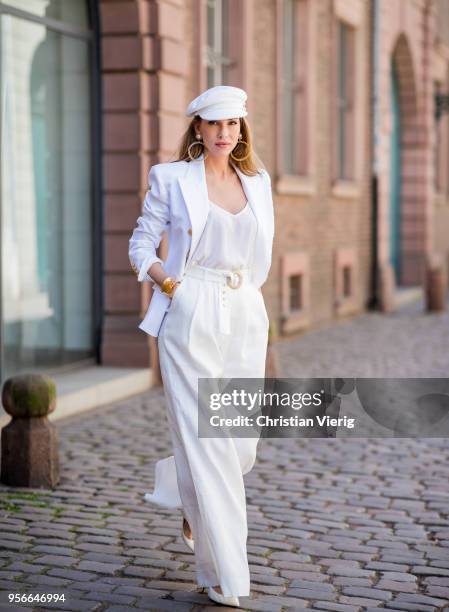 Alexandra Lapp wearing a white cotton blazer with gold buttons by Balmain, linen Palazzo pants with a high waist belt in white by Zimmermann, a white...