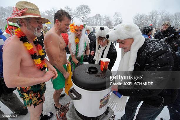 Costumed members of several winter bathing associations warm up after taking the annual bath in the frozen Orankesee lake on January 10, 2010 in...