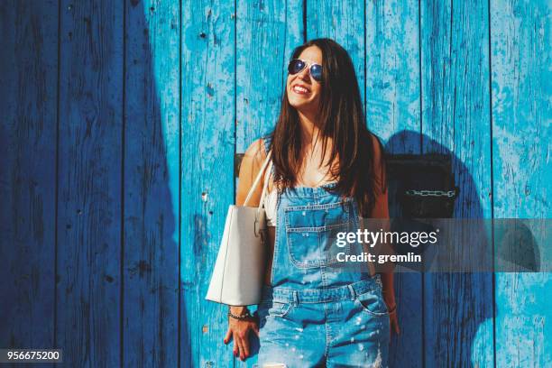 happy fashionable woman leaning on old wooden door - blue purse stock pictures, royalty-free photos & images