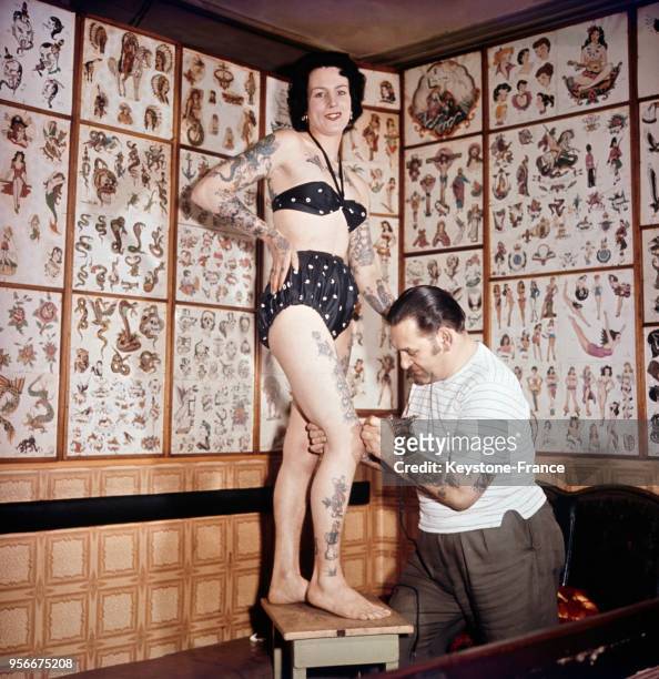 Une jeune femme en maillot de bain se fait dessiner un tatouage par le célèbre tatoueur Les Skuse.